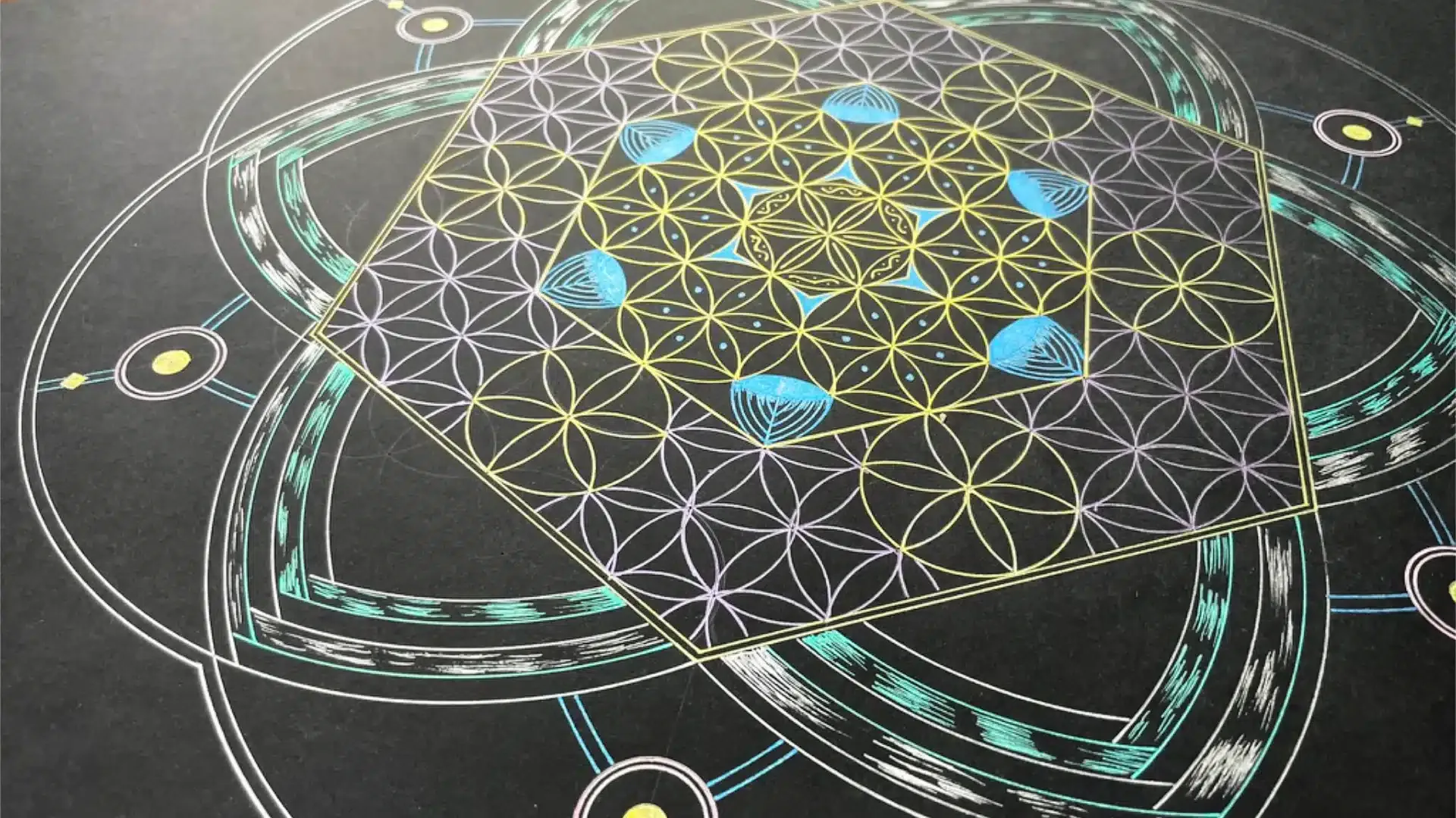 Nahaufnahme eines handgemalten Seelengeometrie-Kunstbilds auf schwarzem Papier: eine Blume des Lebens aus goldenen und violetten Linien in einem gedrehten Quadrat, umgeben von türkisen Ringen und blauen Akzenten